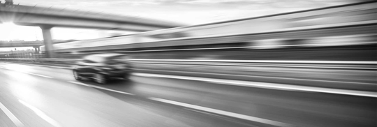 Motion blur depicts a car speeding on a highway under a bridge.