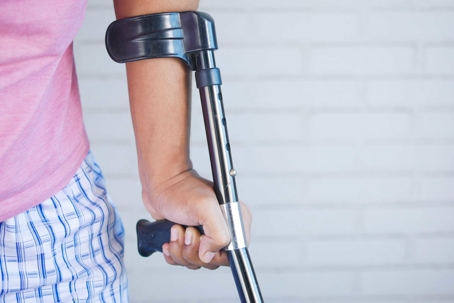 A person with an injury uses a forearm crutch for support, holding the handle with their hand.