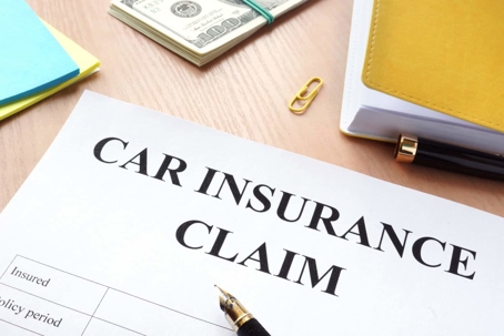 A "Car Insurance Claim" form lies on a desk next to cash, a notebook and pen.