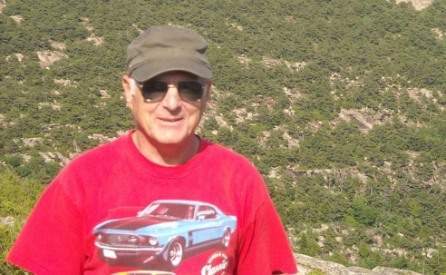 An older man in a red t-shirt stands outdoors.