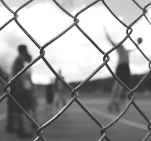 Individuals playing volleyball behind a chain link fence in black and white